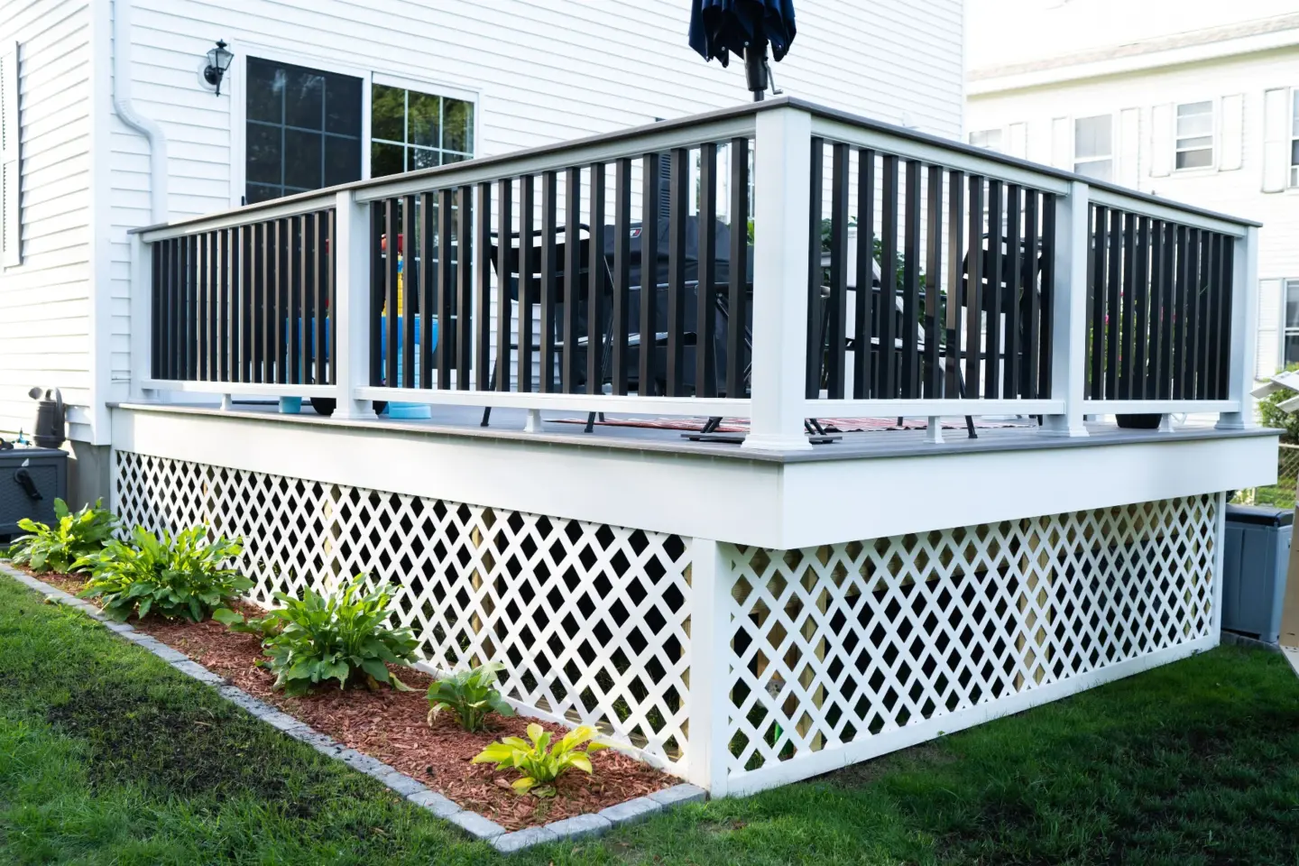 White Deck Surrounded by a White Skirting Featuring a Lush Green Lawn and a House in the Background